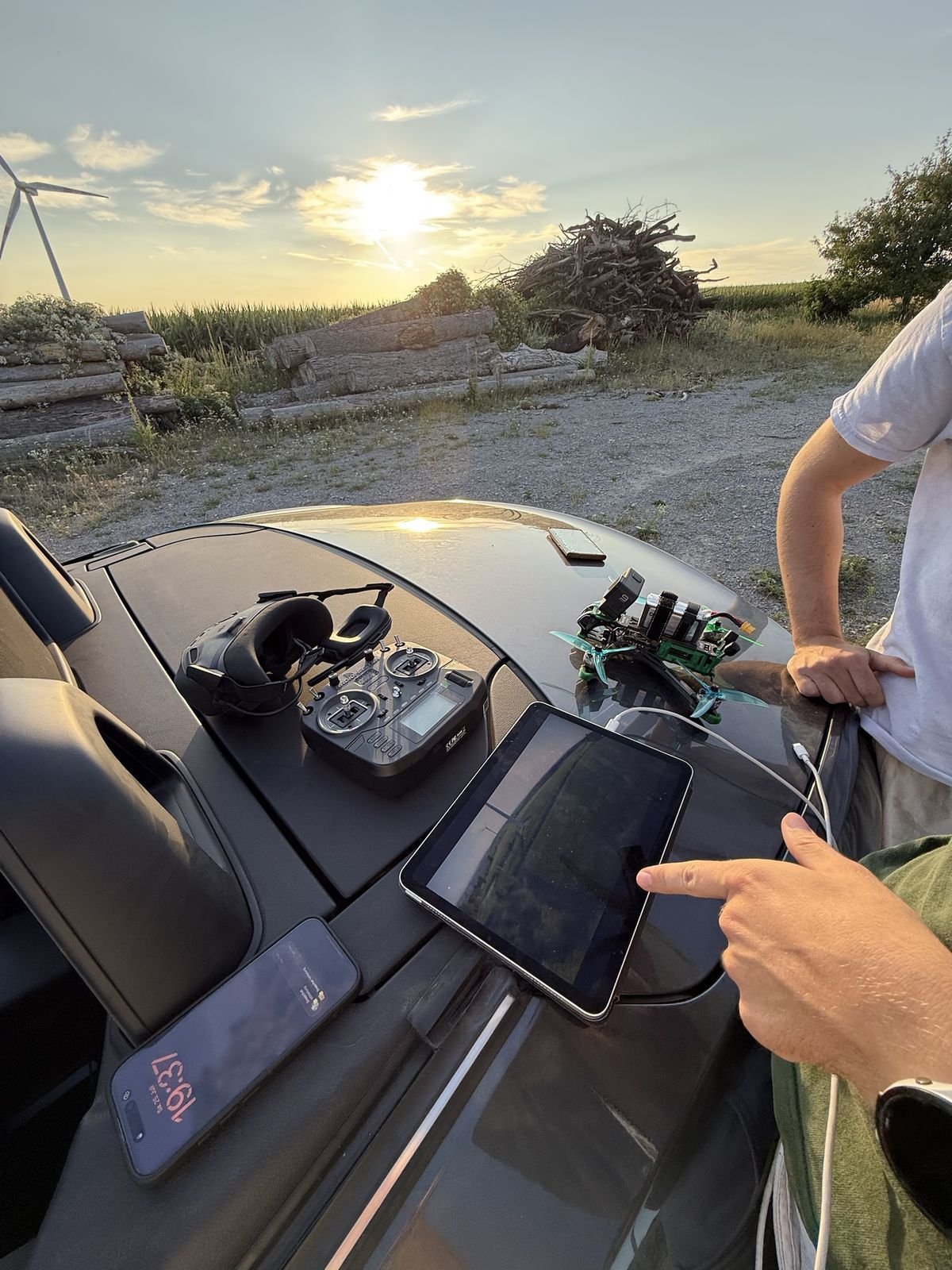 FPV-Drohne, Brille und Fernsteuerung auf einem Auto am Feldweg bei Sonnenuntergang
