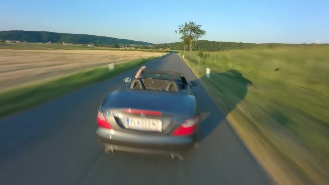 FPV-Aufnahme: offener Mercedes SLK auf einer Landstraße zwischen Feldern, fertig gegradet