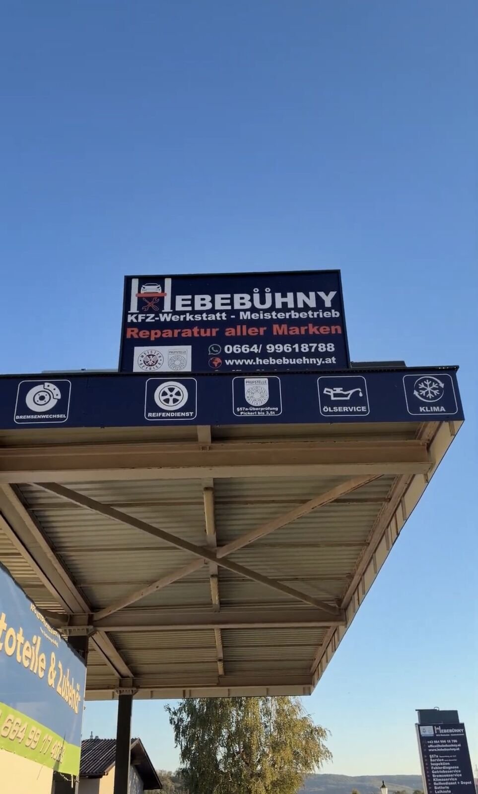 Firmenschild von Hebebühny mit den Leistungen der Werkstatt vor blauem Himmel