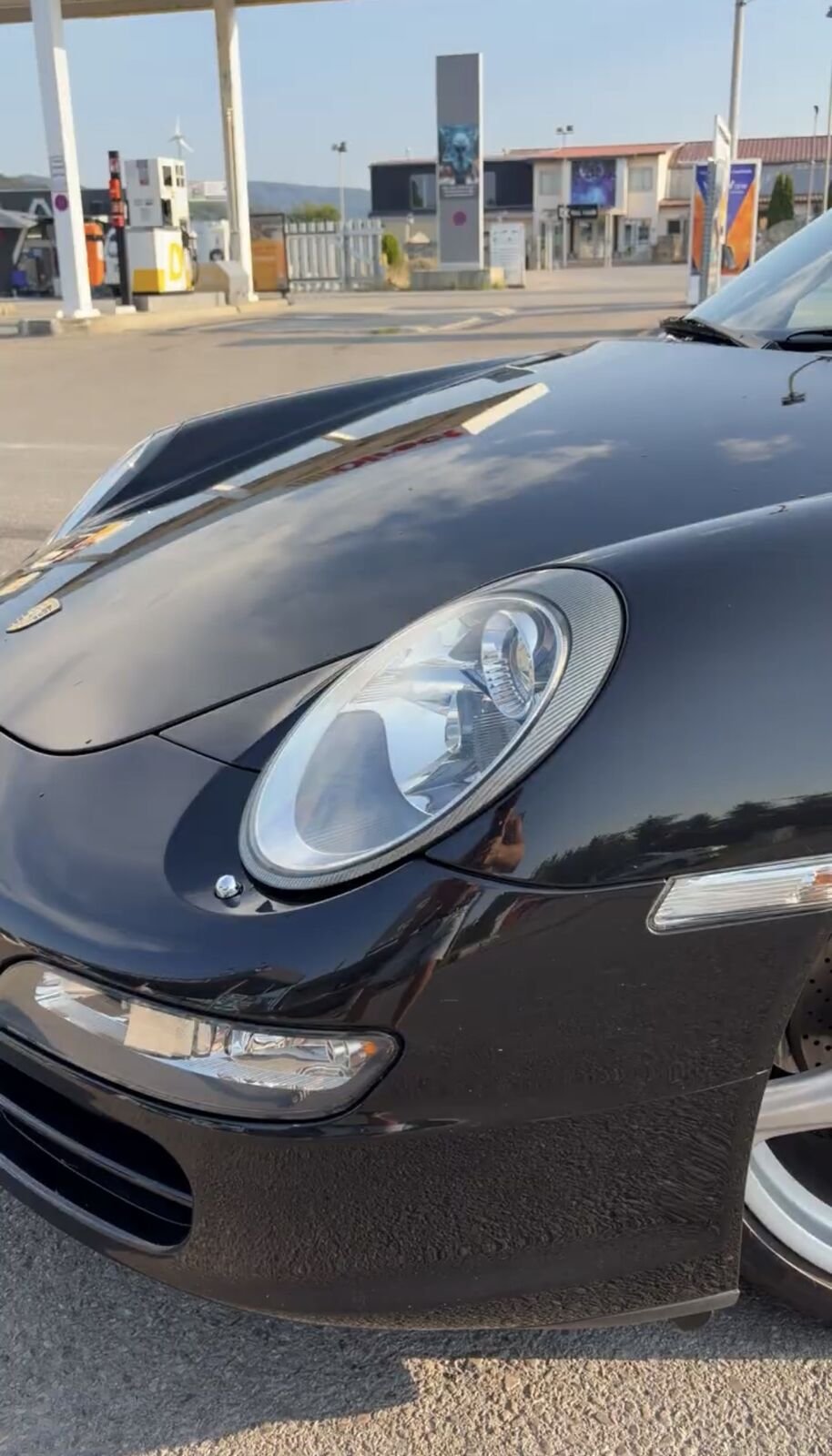 Nahaufnahme vom Scheinwerfer des schwarzen 911 an einer Tankstelle