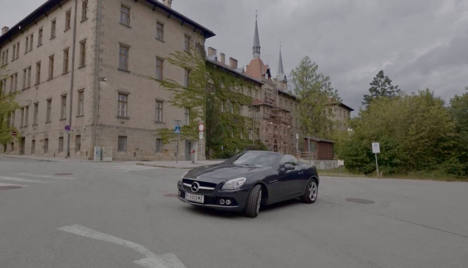 Dunkelgrauer Mercedes SLK auf einer Kreuzung vor einem historischen Gebäude