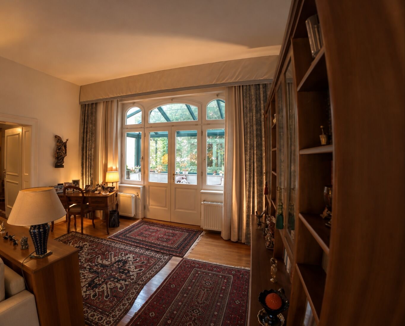 Wohnzimmer der Villa in Graz mit Perserteppichen, Bücherregal und Flügeltür zum Wintergarten