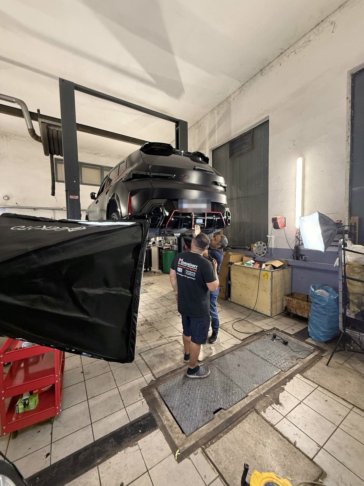 Mechaniker unter einem BMW auf der Hebebühne, davor eine Softbox
